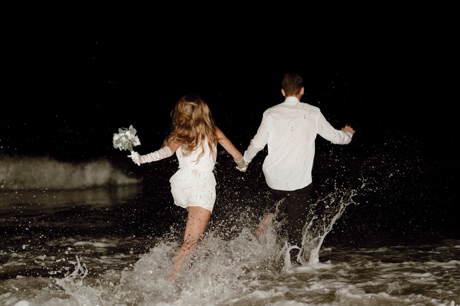 Bride and Groom running into ocean at night
