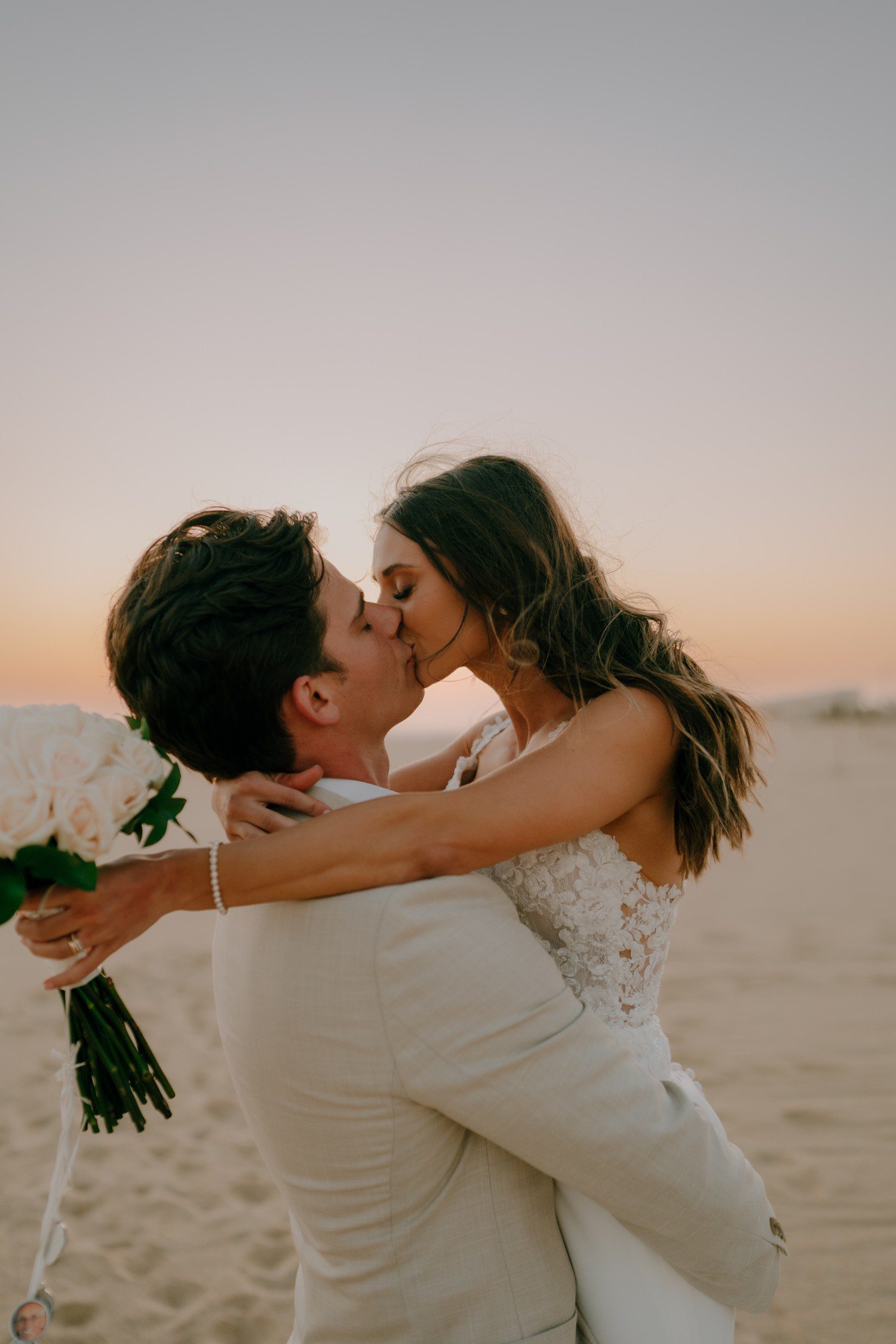 Bride and groom kissing during wedding photos on beach in Los Cabos. 