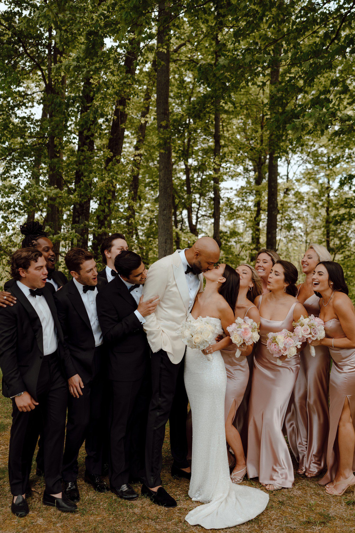 Bride and groom kissing surrounded by wedding party at Saratoga National Golf Club. 