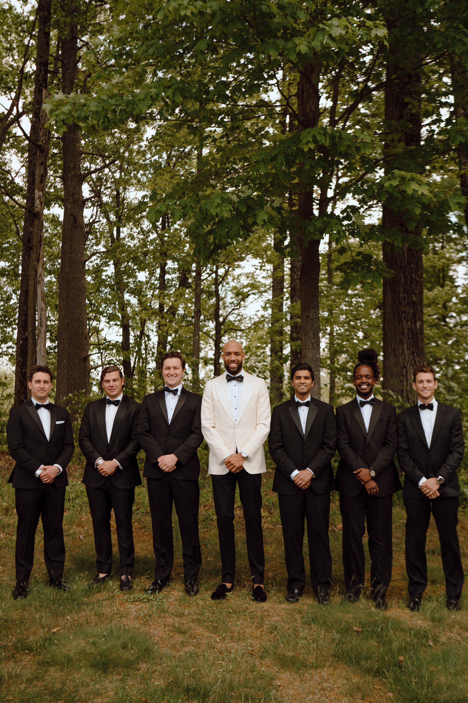Groom in white suit jacket with groomsmen in all black. 