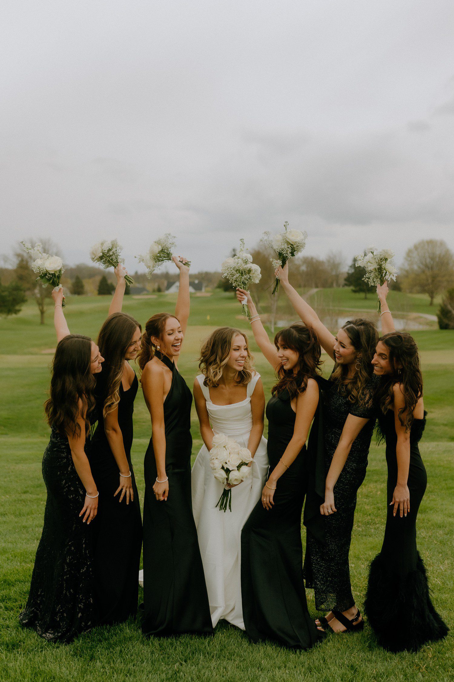 Bridesmaids in black dresses with bride in white with white bouquet. 