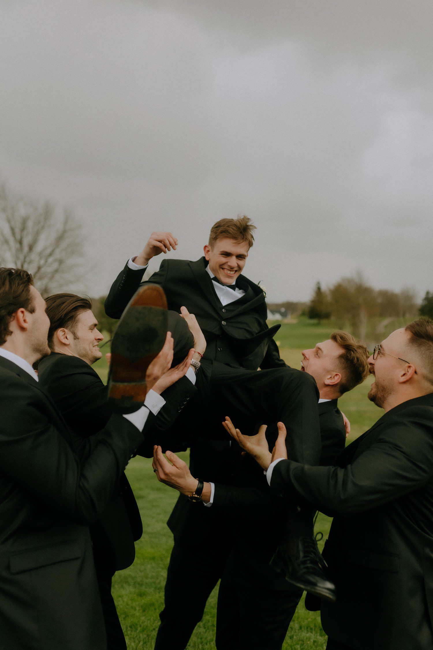 Groomsmen tossing groom in air. 