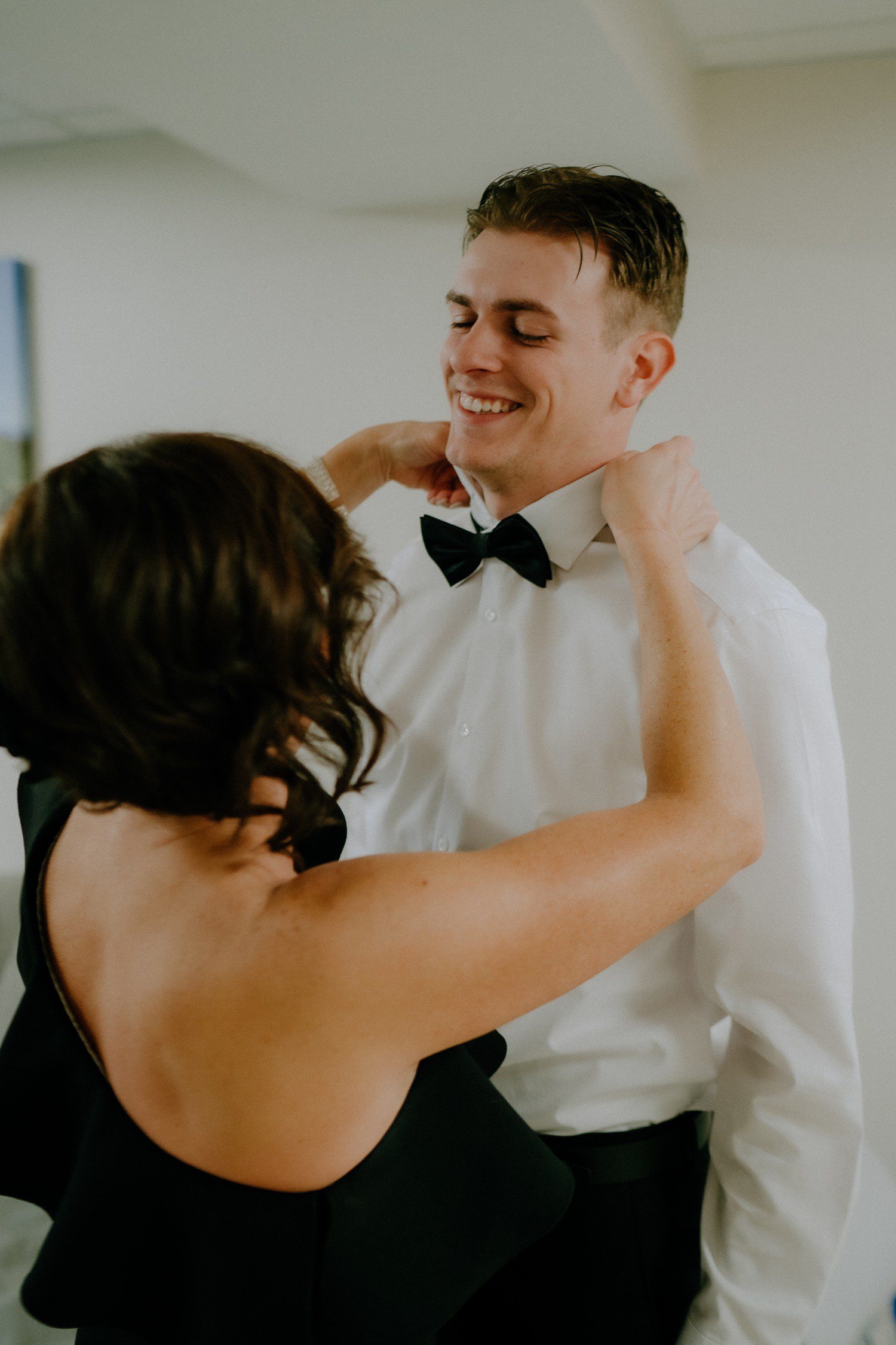 Mother of groom putting on bow tie. 