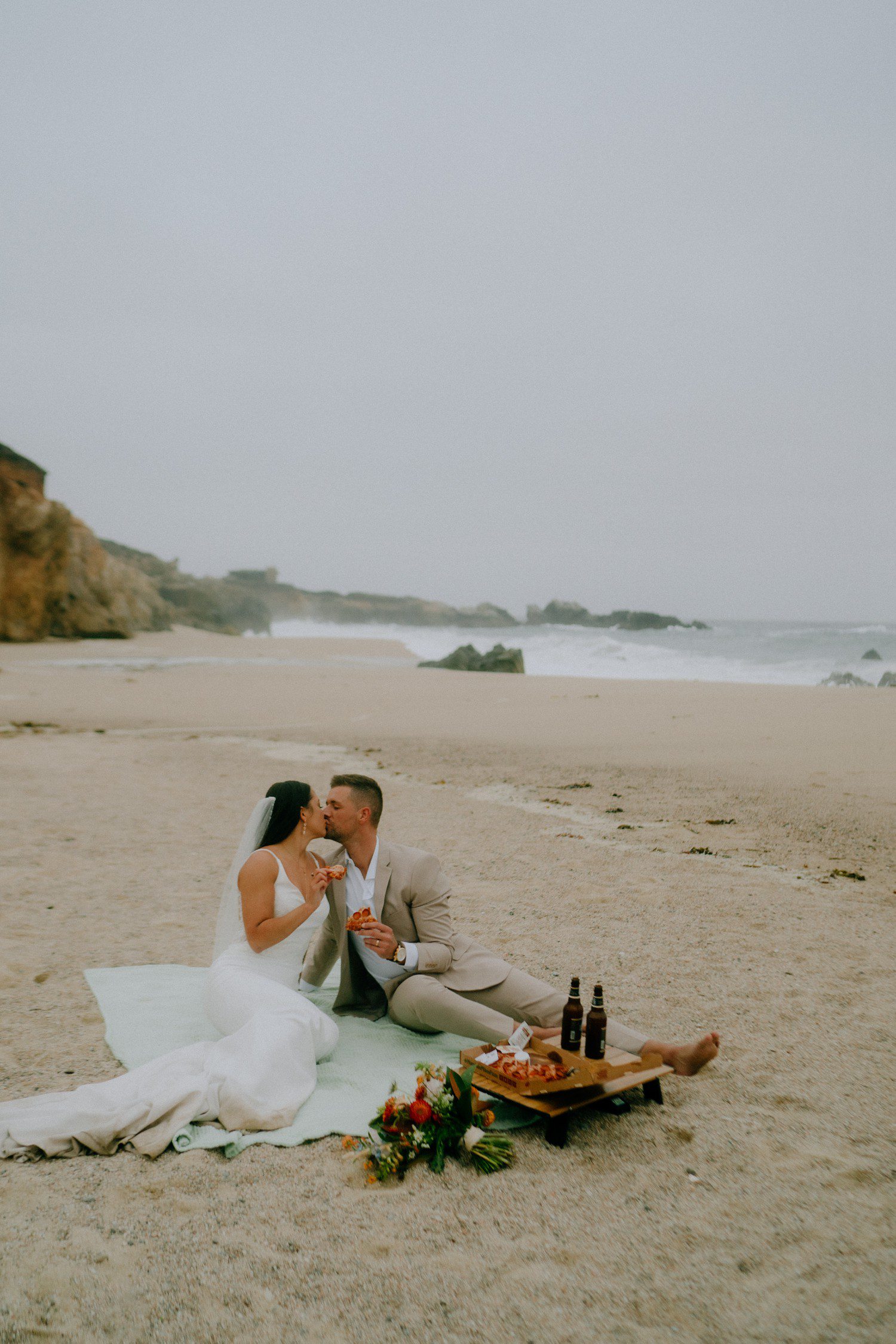 Couple enjoying pizza and beers on the beach for Big Sur elopement.