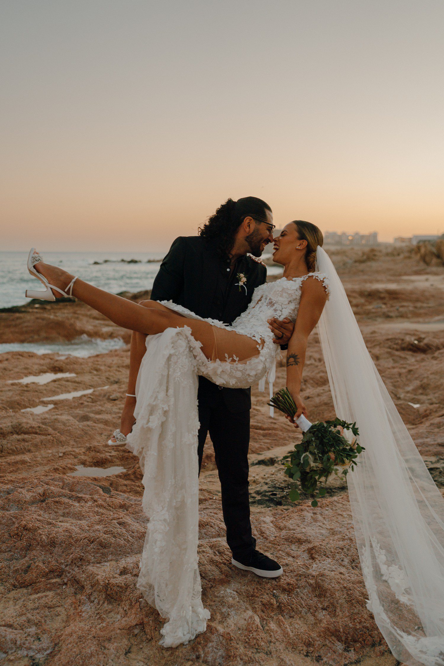 Sunset wedding photos of groom holding bride at Hacienda Del Mar in Los Cabos. 