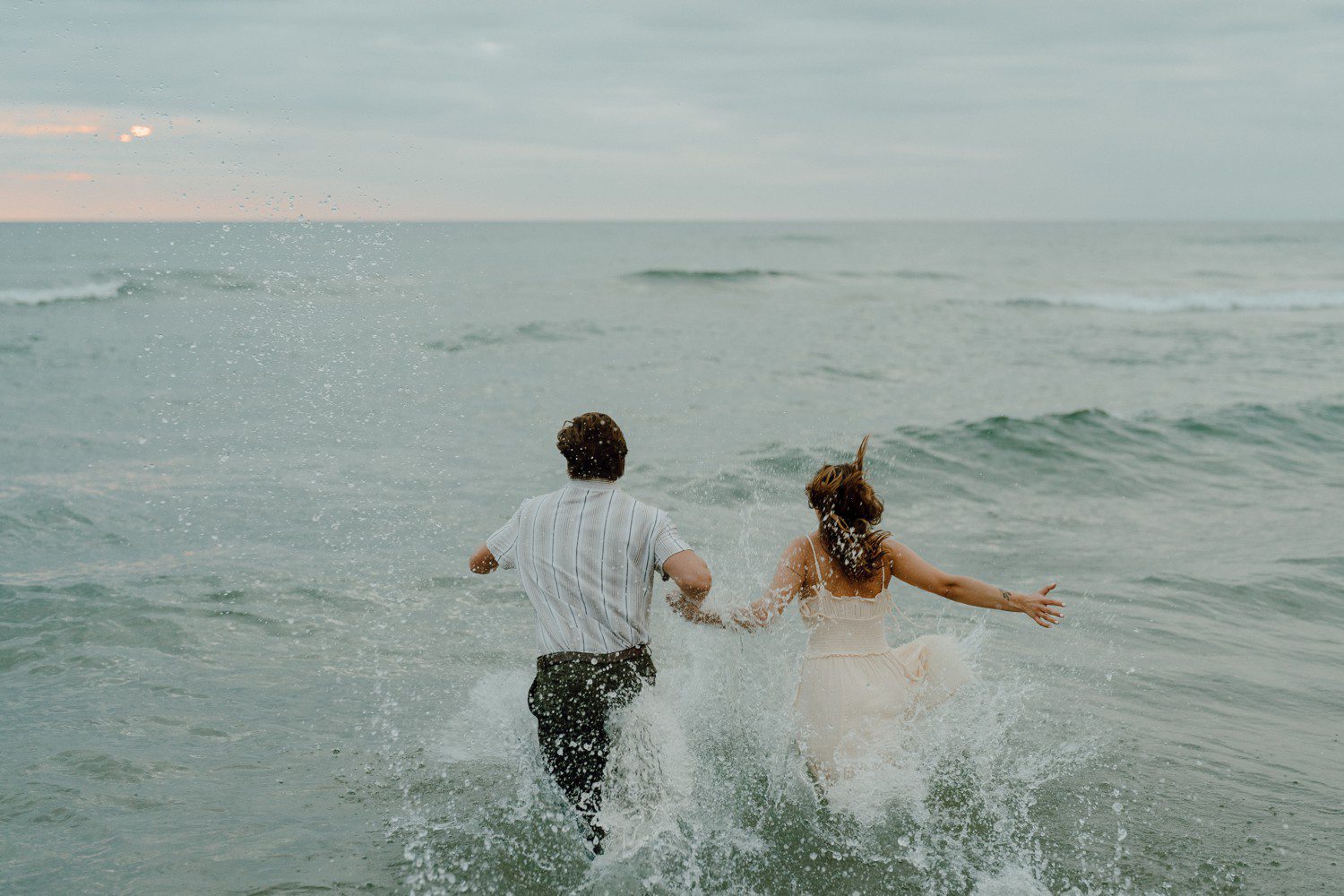 Couple running into the water for beach engagement photos at Lake Michigan Holland State Park.