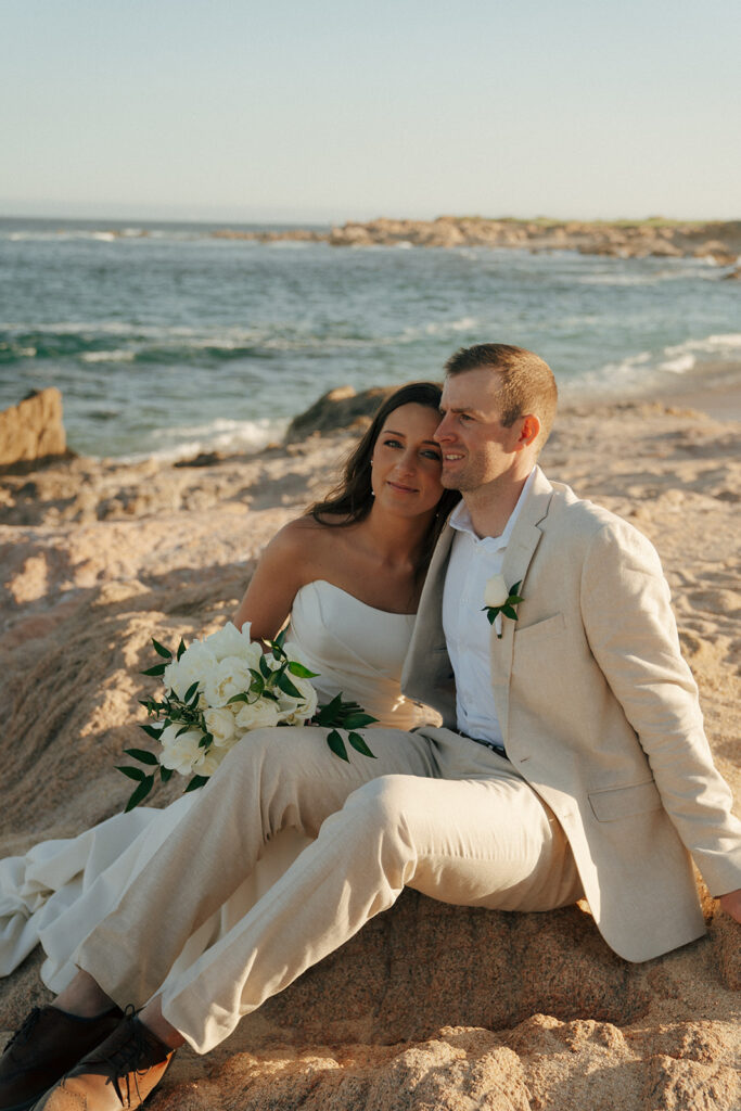 cute portrait if the bride and groom sitting at the beach