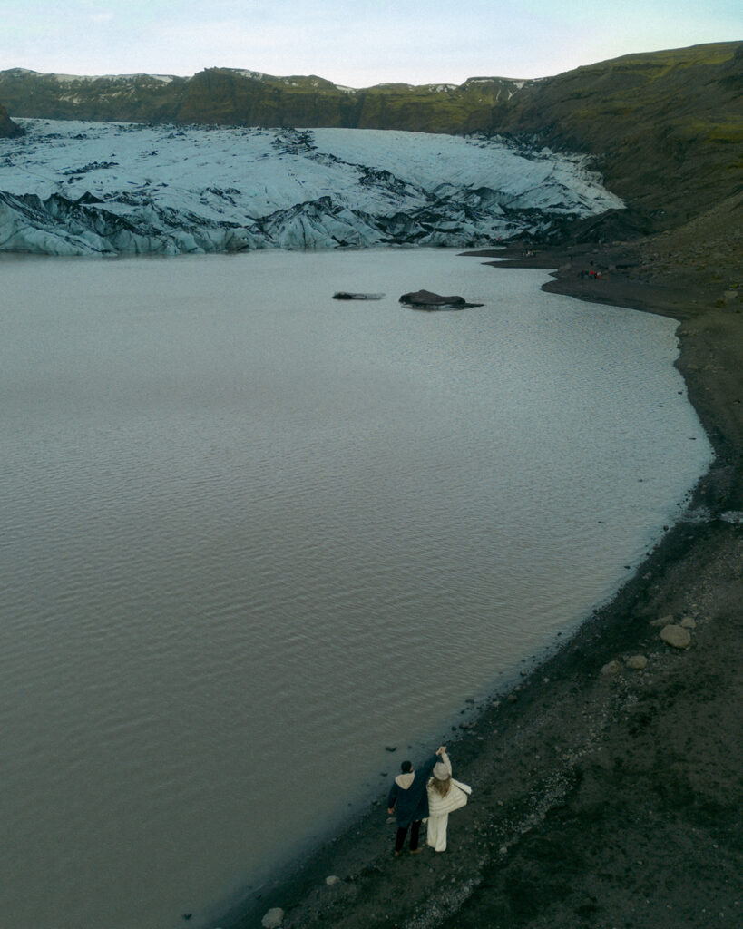 Detail shot of couple holding hands with engagement ring visible against backdrop of blue glacier ice in Iceland photographed by Grand Rapids engagement photographer