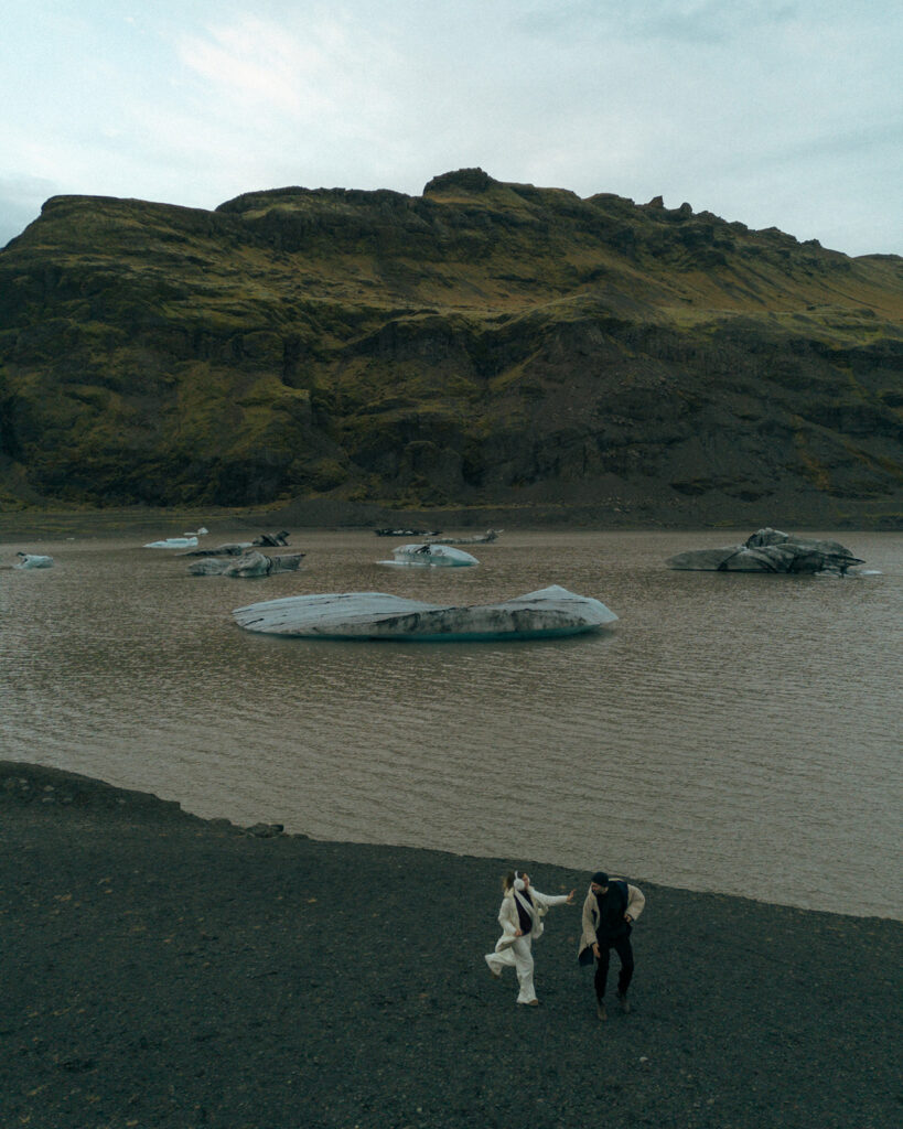 Wide cinematic shot of small couple silhouette on enormous Iceland glacier showcasing scale and beauty captured by destination Iceland engagement photographer