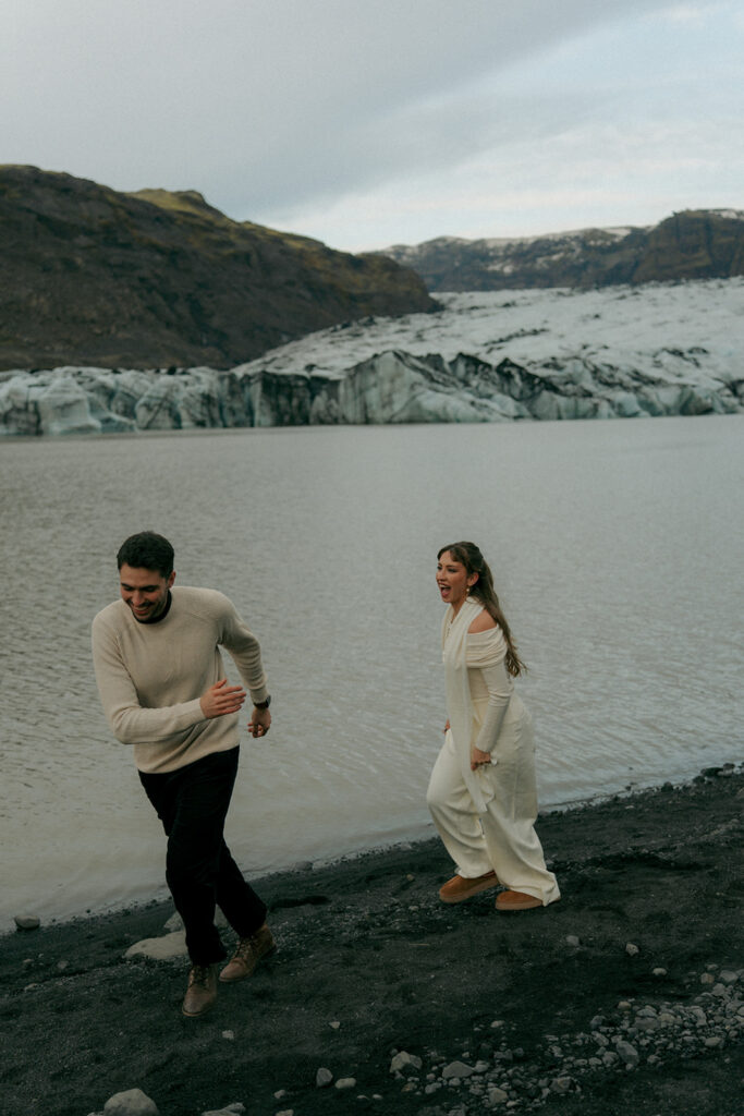 Couple sitting together on edge of glacier ice formation in Iceland during sunrise engagement session with Grand Rapids based Iceland engagement photographer