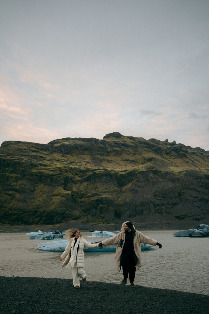 Engaged couple standing in ice cave with brilliant blue glacier walls during Iceland engagement photo session with Grand Rapids destination photographer