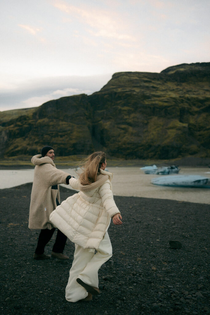 Couple holding hands walking across blue ice formations on Iceland glacier captured by Grand Rapids engagement photographer specializing in Iceland elopements