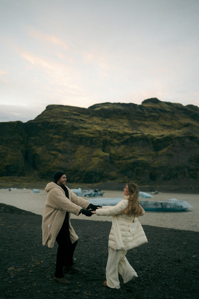 Couple kissing on glacier overlook with Iceland mountain range and valley view in background photographed by Michigan Iceland engagement photographer specializing in adventure sessions