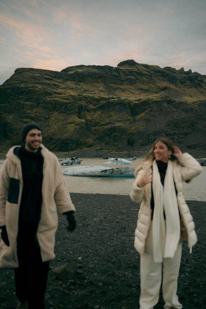 Engaged woman in flowing dress standing on Iceland glacier ice while fiance holds her hand photographed by Michigan based Iceland engagement photographer
