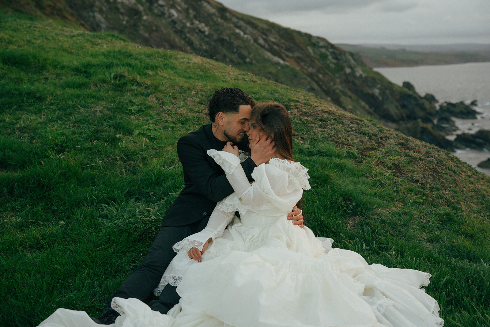 Groom holding bride on rocky cliffs elopement photos overlooking ocean Fast Castle Scotland