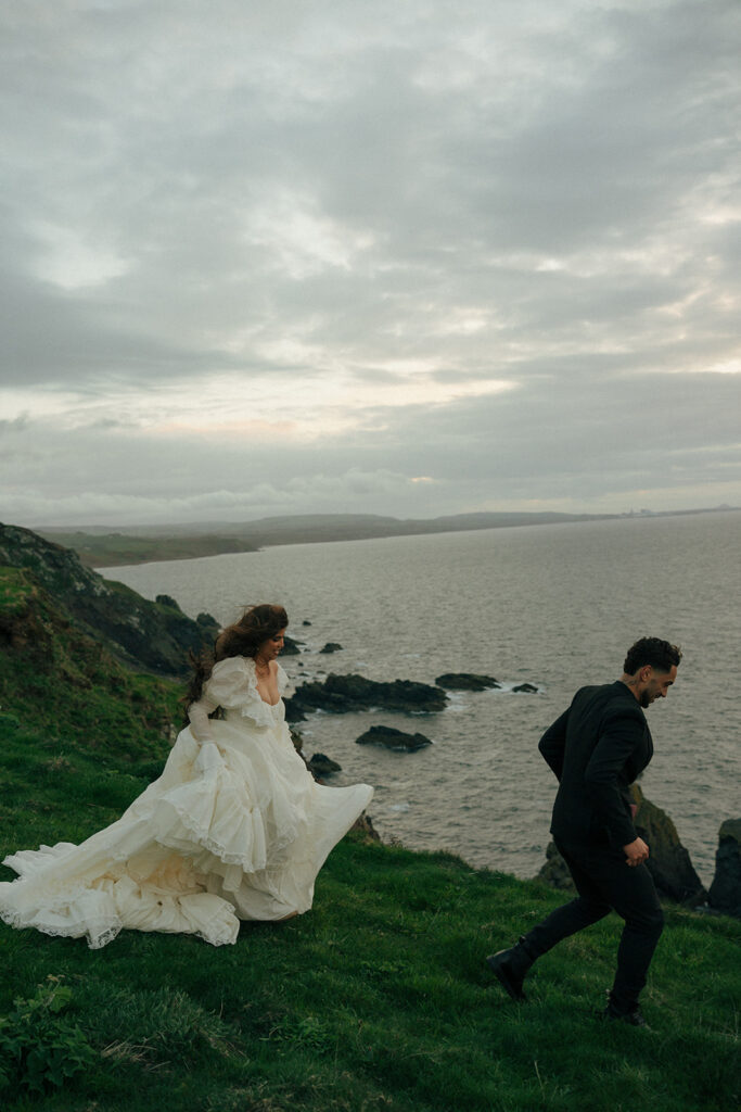 Couple walking hand in hand on coastal path during cliffs elopement photos Fast Castle Edinburgh