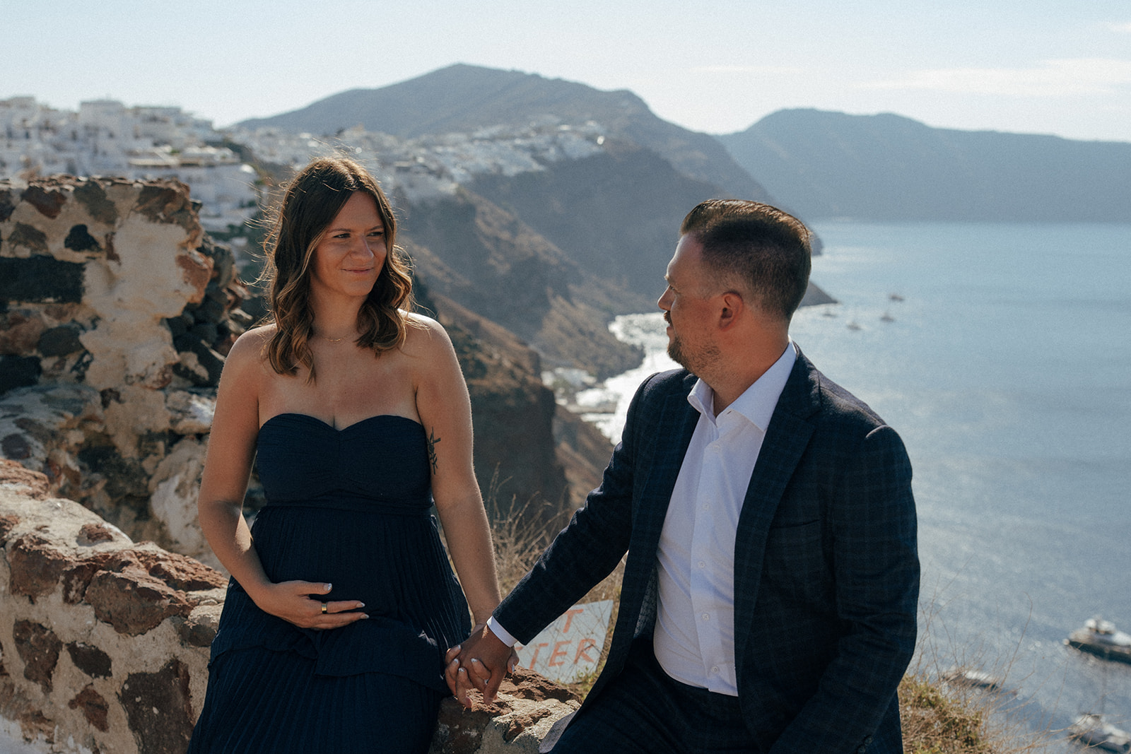 Maternity couple embracing on terrace with Santorini caldera and sunset sky background