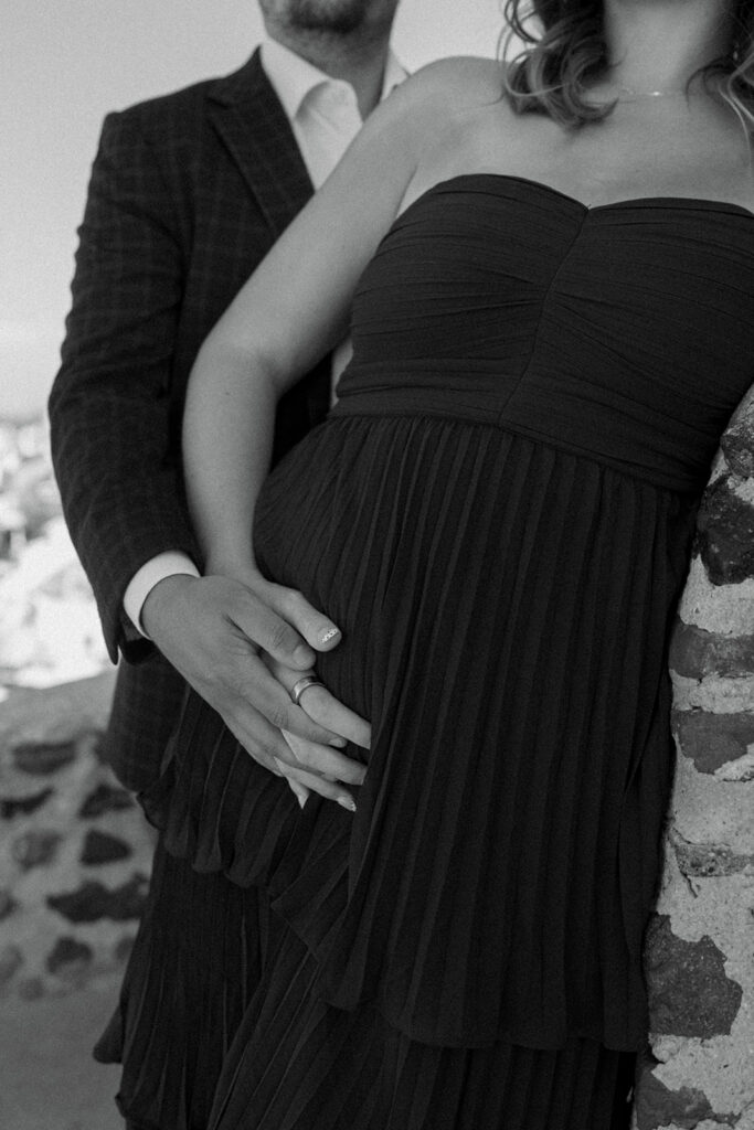 Expecting couple laughing together with iconic Santorini windmill and Aegean Sea view
