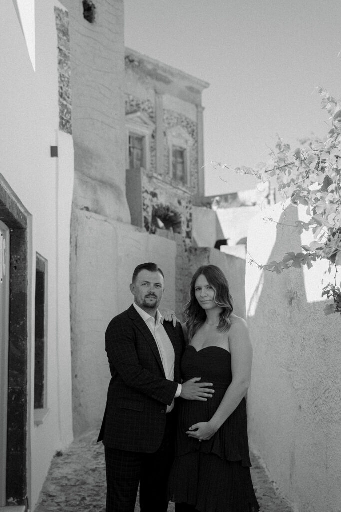 Couple walking through narrow white washed streets of Oia during Greece maternity session