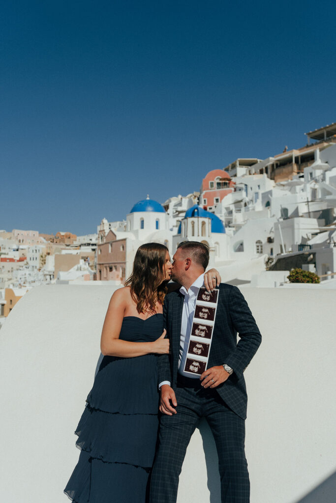 Close up of pregnant belly with Santorini white architecture and blue doors behind