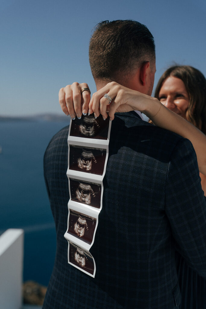Couple dancing on rooftop terrace with panoramic Santorini caldera views during maternity shoot