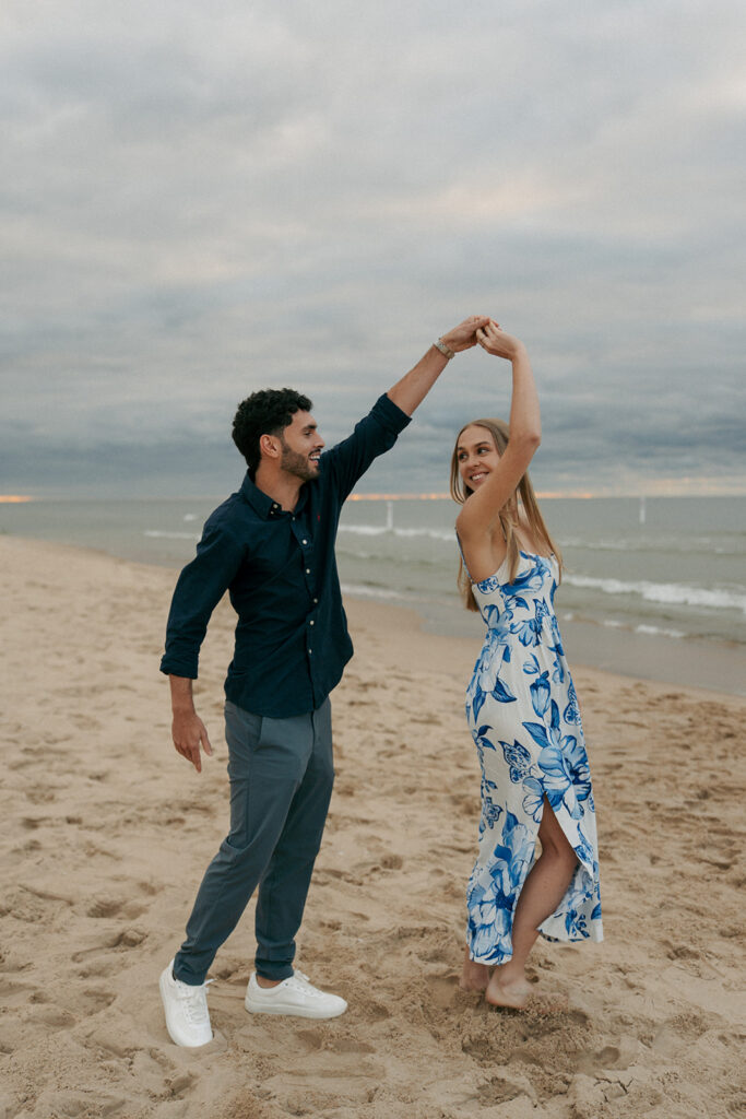 Couple twirling and dancing on Oval Beach sand dunes during engagement photos