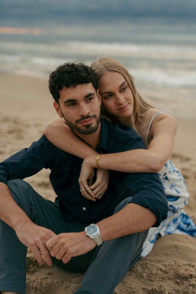 Wide shot of couple on empty Oval Beach with dunes and sky during engagement