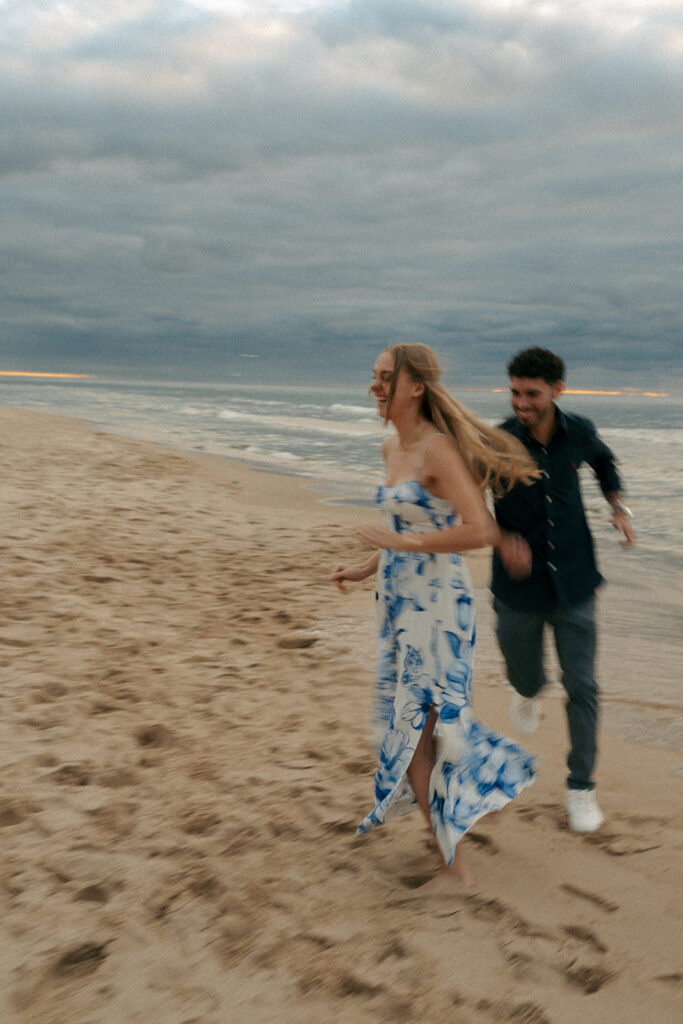 Couple celebrating engagement with champagne on Oval Beach at sunset Saugatuck Michigan