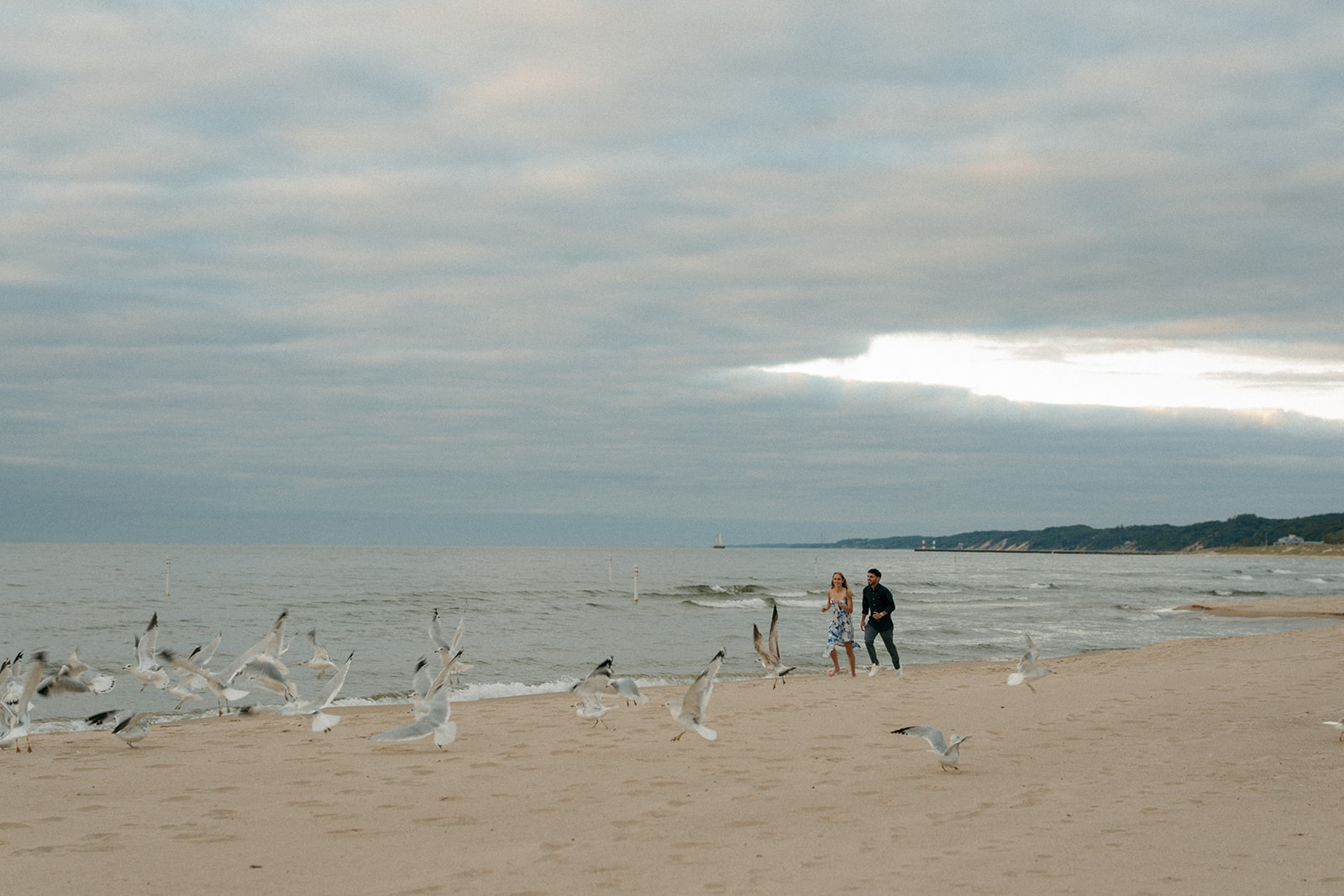 Newly engaged couple laughing together on Oval Beach dunes in golden sunset light