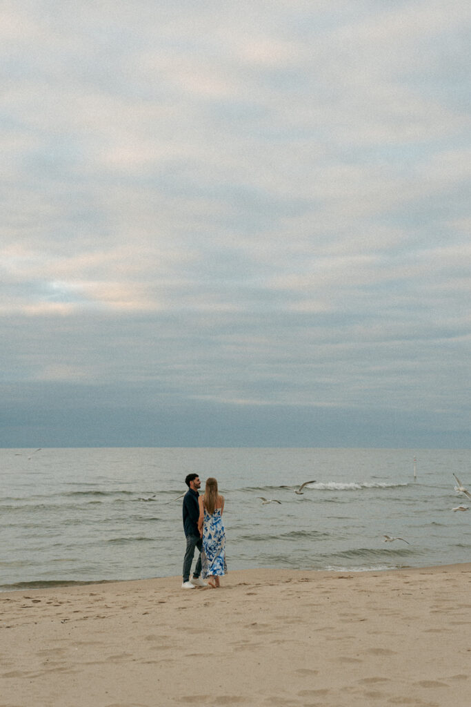 Silhouette of engaged couple holding hands at Oval Beach during romantic Michigan sunset