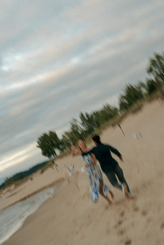 Newly engaged couple sitting together on Oval Beach sand at sunset Saugatuck