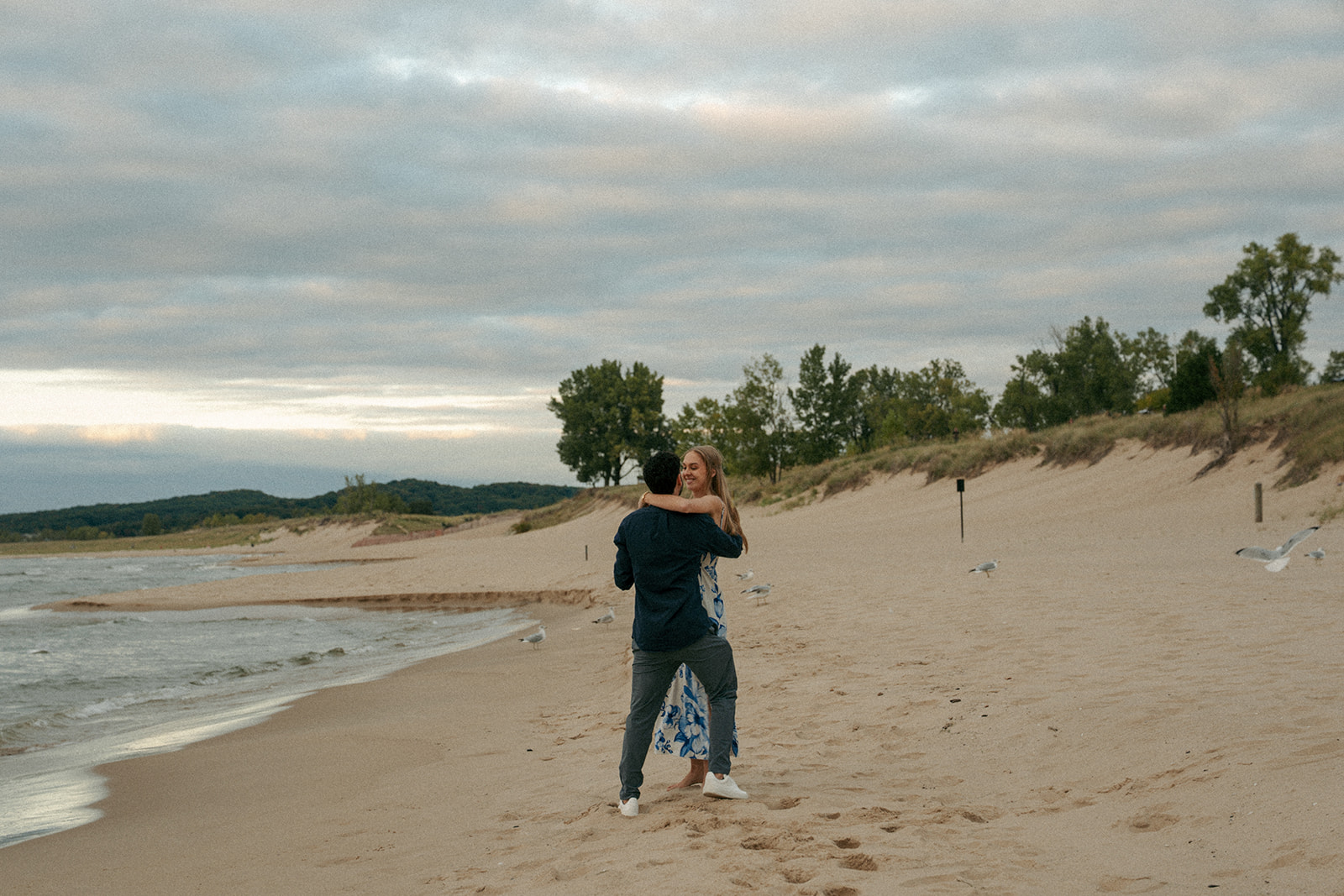Couple embracing during sunset proposal at Oval Beach in Saugatuck Michigan
