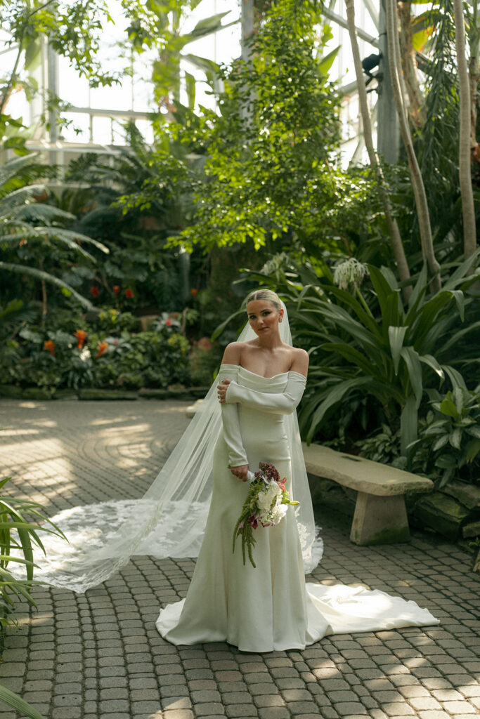 Bride holding white and green bouquet surrounded by tropical plants at Grand Rapids wedding venue