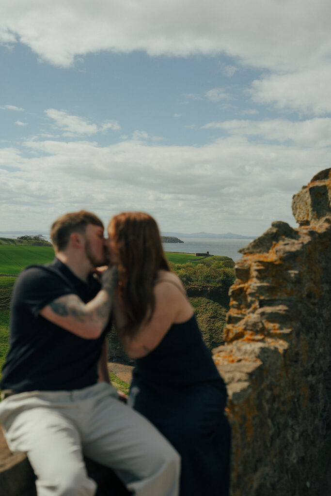 Engaged couple kissing at sunset with Scottish coastal cliffs behind them Tantalon